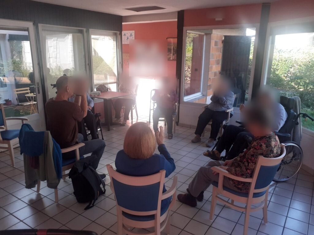 Atelier de yoga sur chaise : des résidents assis en cercle lèvent les bras avec l'animateur